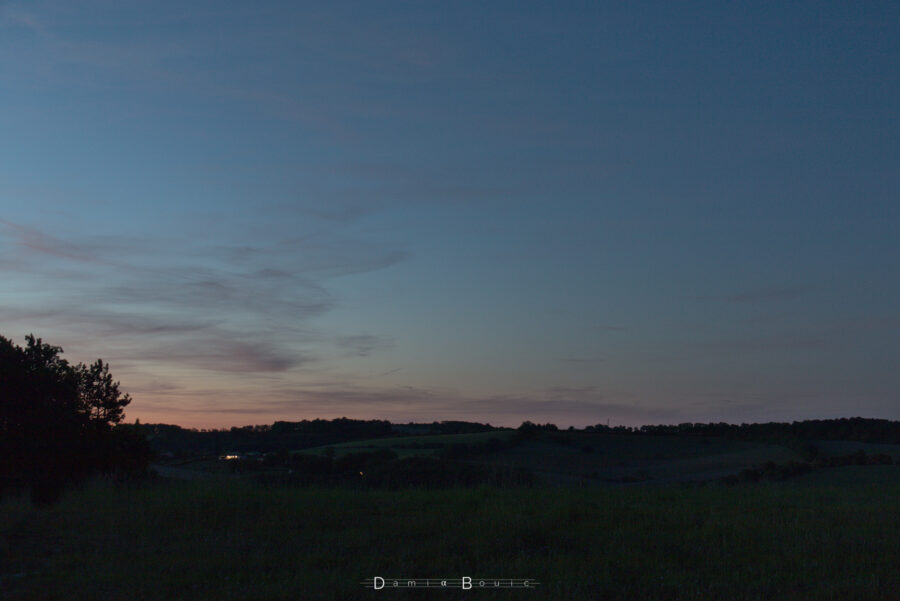 Paysage doucement vallonné dans les dernières lueurs du crépuscule, quelques cirrus strient le ciel à gauche