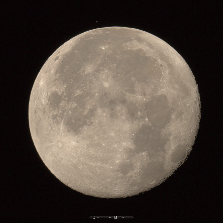 La Lune presque pleine, avec en haut, proche du limbe, la planète Saturne, assez sombre en comparaison, dont on peut distinguer les anneaux presque par la tranche