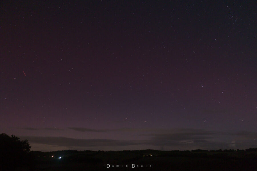 Portion de ciel nocturne, montrant le Nord, avec étoiles et nuages, qui ressortent sur un fond plus clair proche de l'horizon