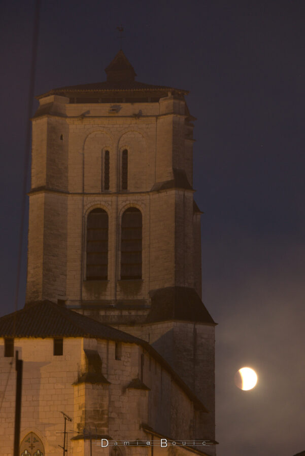 Un clocher massif, bien rectangulaire, tout en pierre, qui trône fièrement près d'une Lune échancrée par l'ombre de la Terre. La Lune semble comme dans un brouillard.